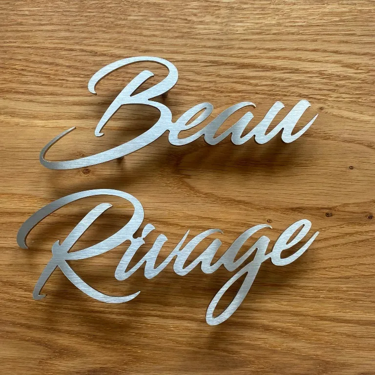 Enseigne « Beau Rivage » en lettres découpées script en inox, présentée sur un plan de bois clair
