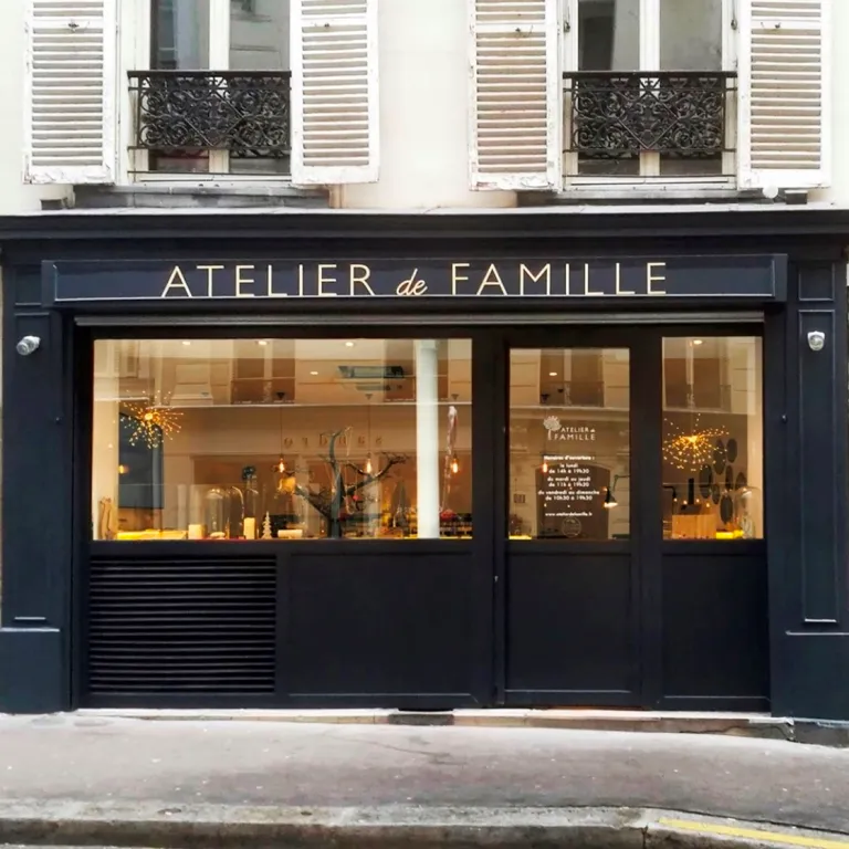 Enseigne de devanture « Atelier de Famille » en lettres laiton brossé doré sur bandeau noir, façade de boutique parisienne