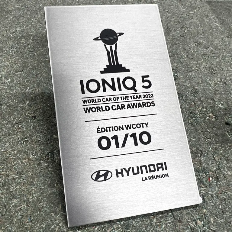 Plaque commémorative en inox brossé gravée d'un logo constructeur automobile et d'une mention d'édition limitée numérotée, posée sur un sol clair