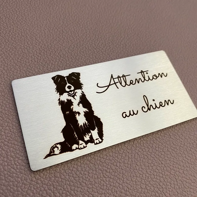 Plaque en inox brossé gravée au laser d'un border collie et de la mention "Attention au chien" en écriture manuscrite, posée sur un fond en cuir