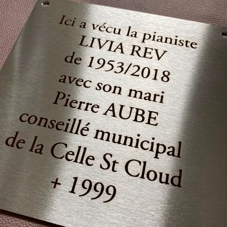 Plaque commémorative carrée en inox brossé gravée au laser d'un texte hommage, percée en haut aux deux coins, posée sur un fond en cuir