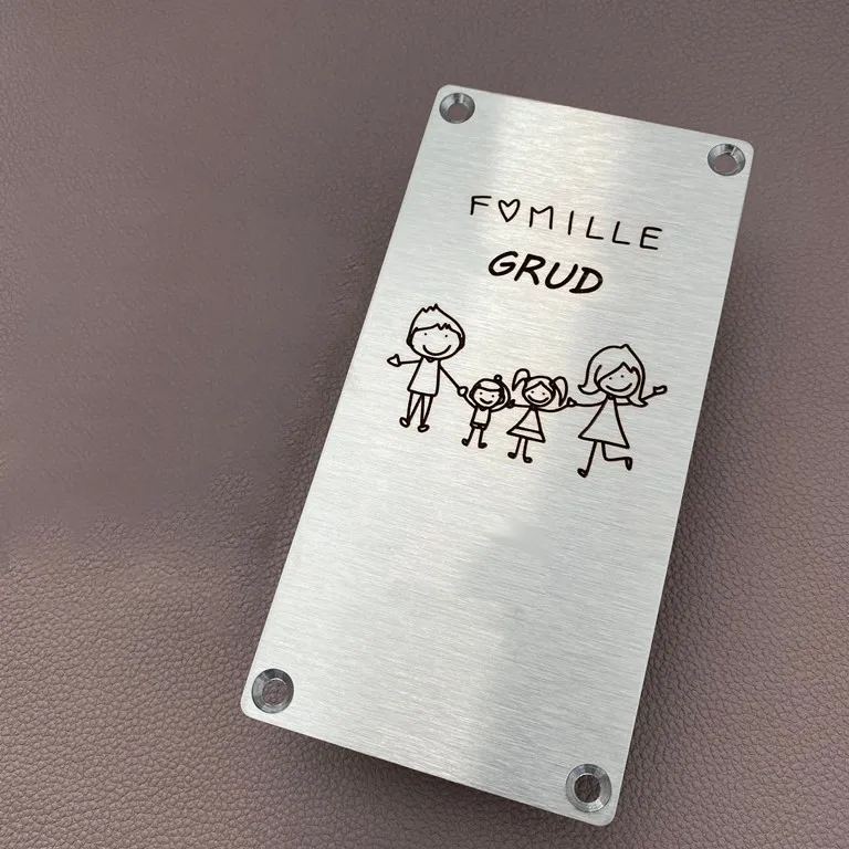 Plaque de maison en inox brossé gravée au laser du nom d'une famille et d'un dessin illustrant parents et enfants, percée aux quatre coins, posée sur un fond en cuir