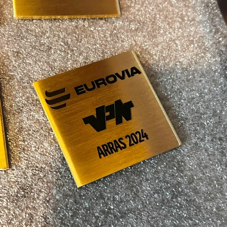 Plaque commémorative carrée en laiton brossé gravée au laser de logos d'entreprises et d'une mention d'événement, posée sur un emballage de protection