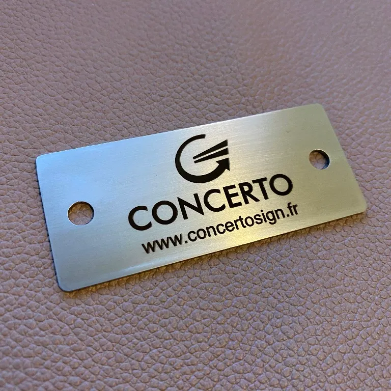 Petite plaque en laiton brossé gravée au laser du logo, du nom et du site web d'une entreprise, percée aux deux extrémités, posée sur un fond en cuir