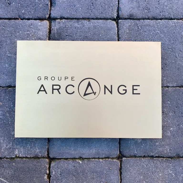 Plaque professionnelle rectangulaire en laiton brossé gravée au laser du logo d'une entreprise, posée sur un sol pavé