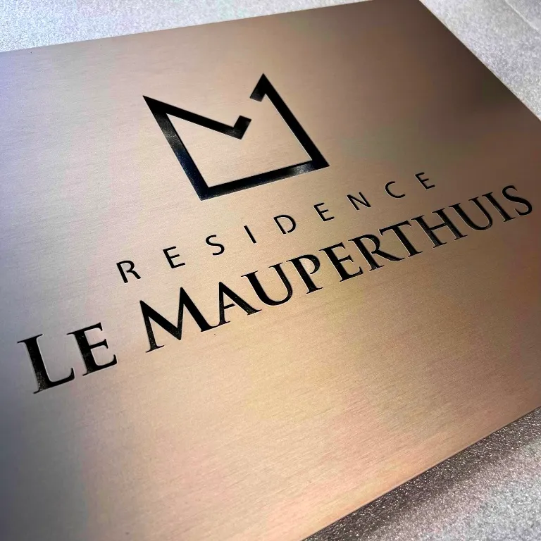 Plaque de résidence en laiton brossé gravée au laser d'un logo couronne et du nom de la résidence, posée sur une surface claire