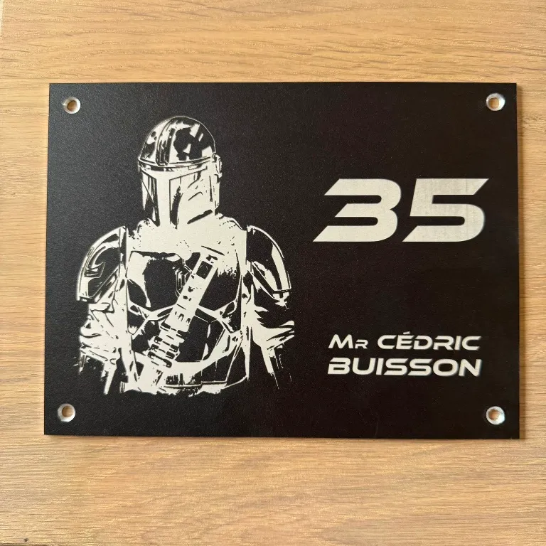 Plaque de maison numéro 35 en finition noire mate, gravure blanche représentant un personnage de guerrier en armure, avec le nom "Mr Cédric Buisson", percée aux quatre coins