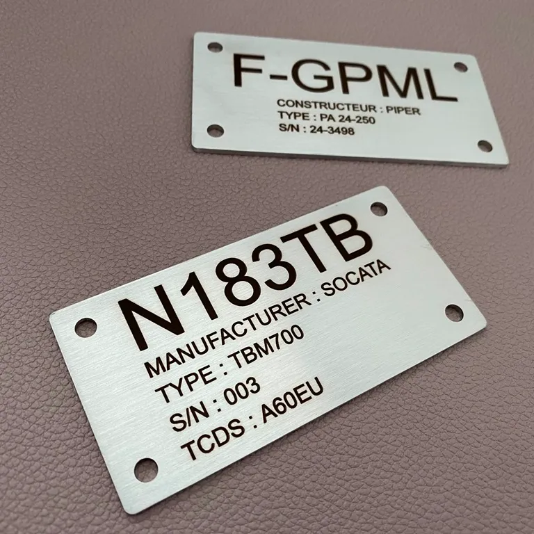 Deux plaques d'identification en inox brossé gravées au laser d'immatriculations et de données techniques d'aéronefs, percées aux quatre coins, posées sur un fond en cuir