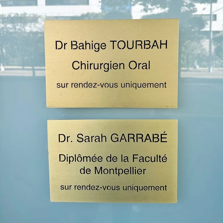 Deux plaques professionnelles en laiton brossé gravées en noir pour des praticiens de santé, fixées sur une porte vitrée