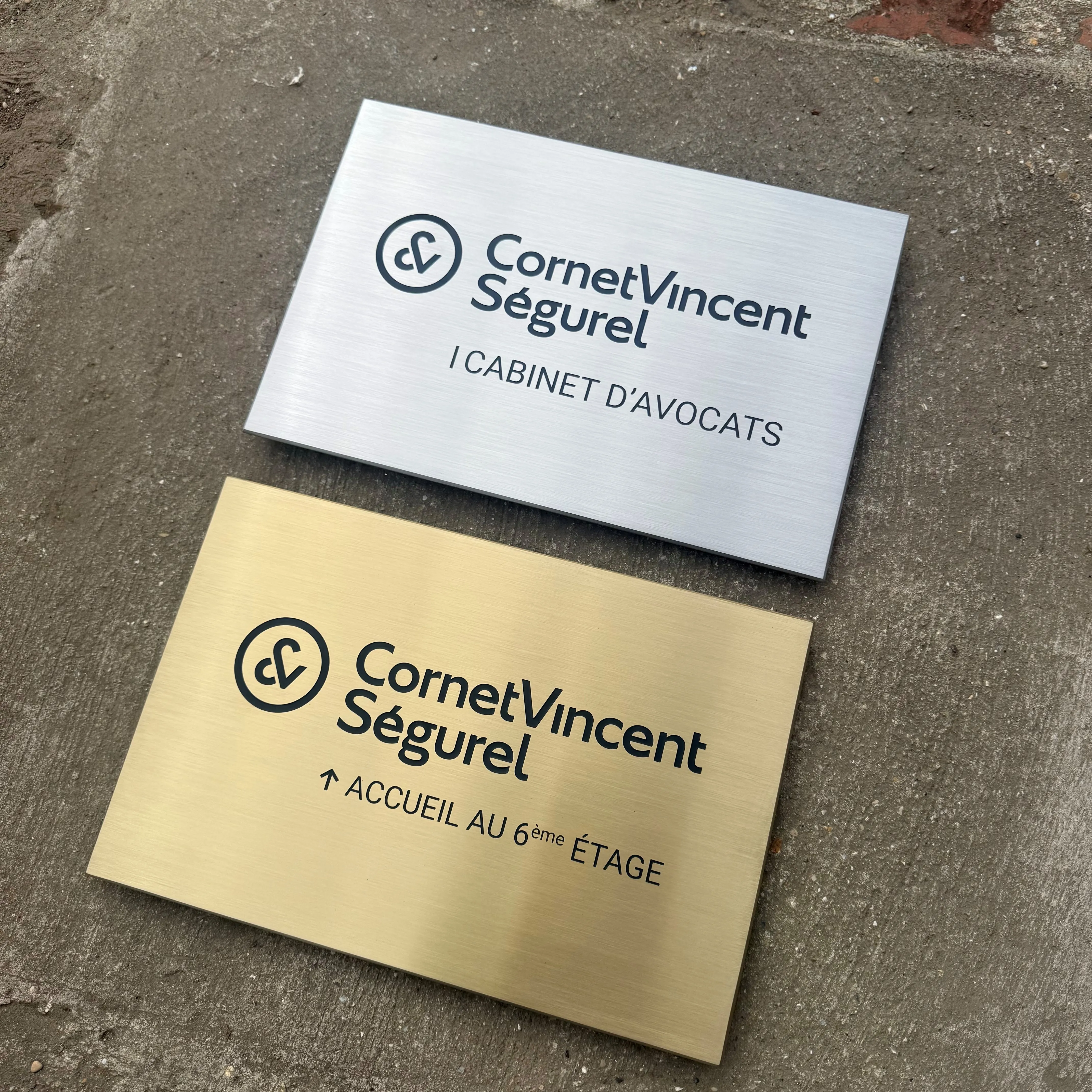 Deux plaques professionnelles de cabinet d'avocats, l'une en inox brossé gris, l'autre en laiton brossé doré, logo et texte gravés fraisés peints en noir